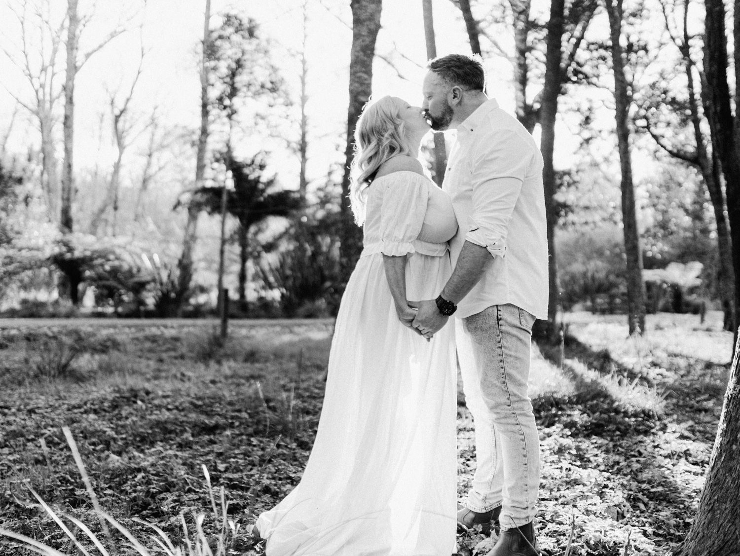 Black and white photo of a couple holding hands in a forest, woman in white gown, man in white shirt.
