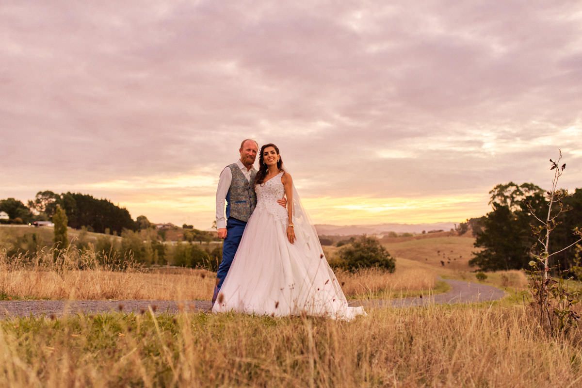 Bride and groom posing together in a golden field at sunset, wearing wedding attire in a romantic countryside setting.