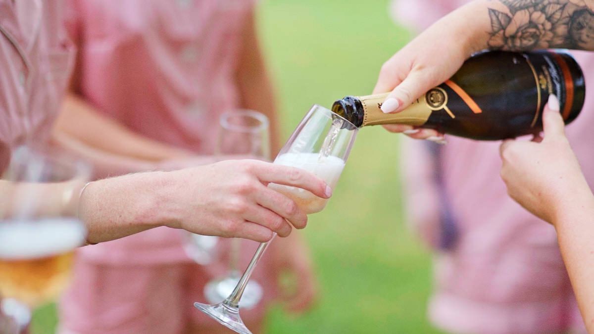 Champagne being poured into a flute glass at an outdoor celebration with guests in pink attire.