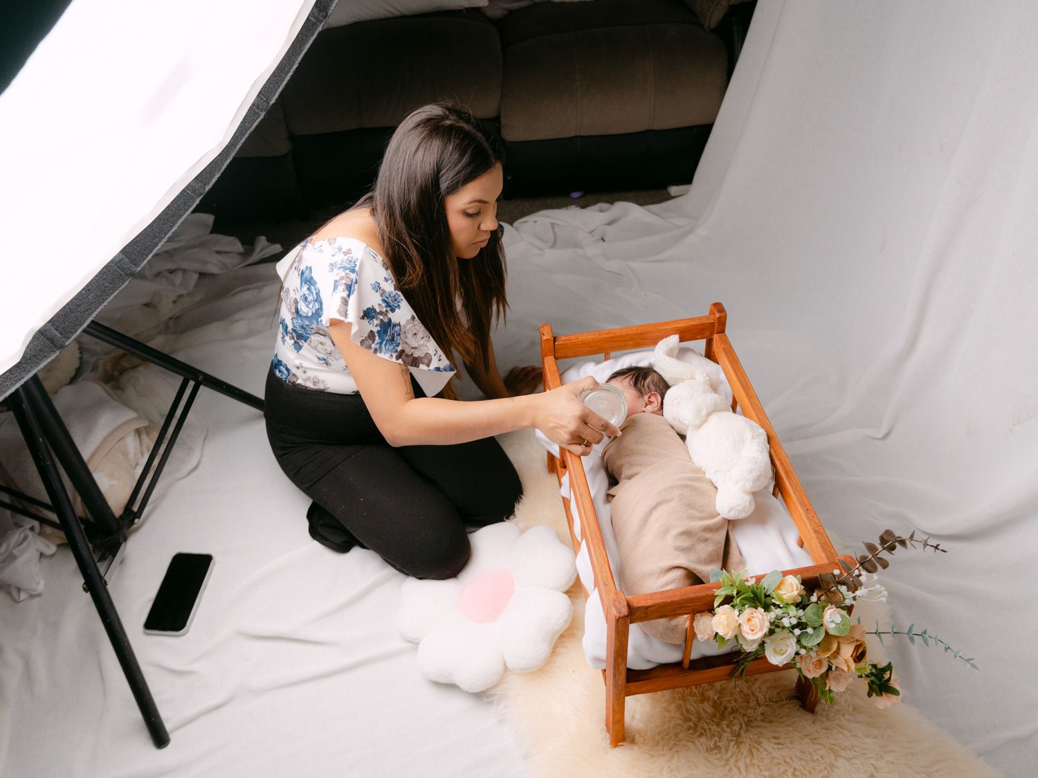 Photographer arranging newborn baby in wooden crib during professional photo shoot with studio lighting setup.