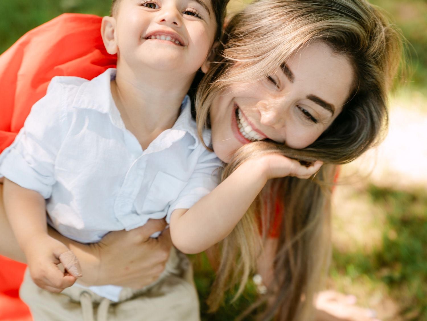 A joyful mother hugging her laughing young son outdoors, both smiling in a warm, candid family moment.