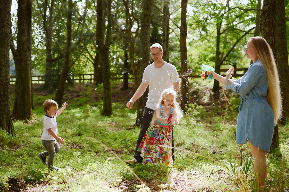 A family of four enjoying a walk together in a lush green woodland on a sunny day.