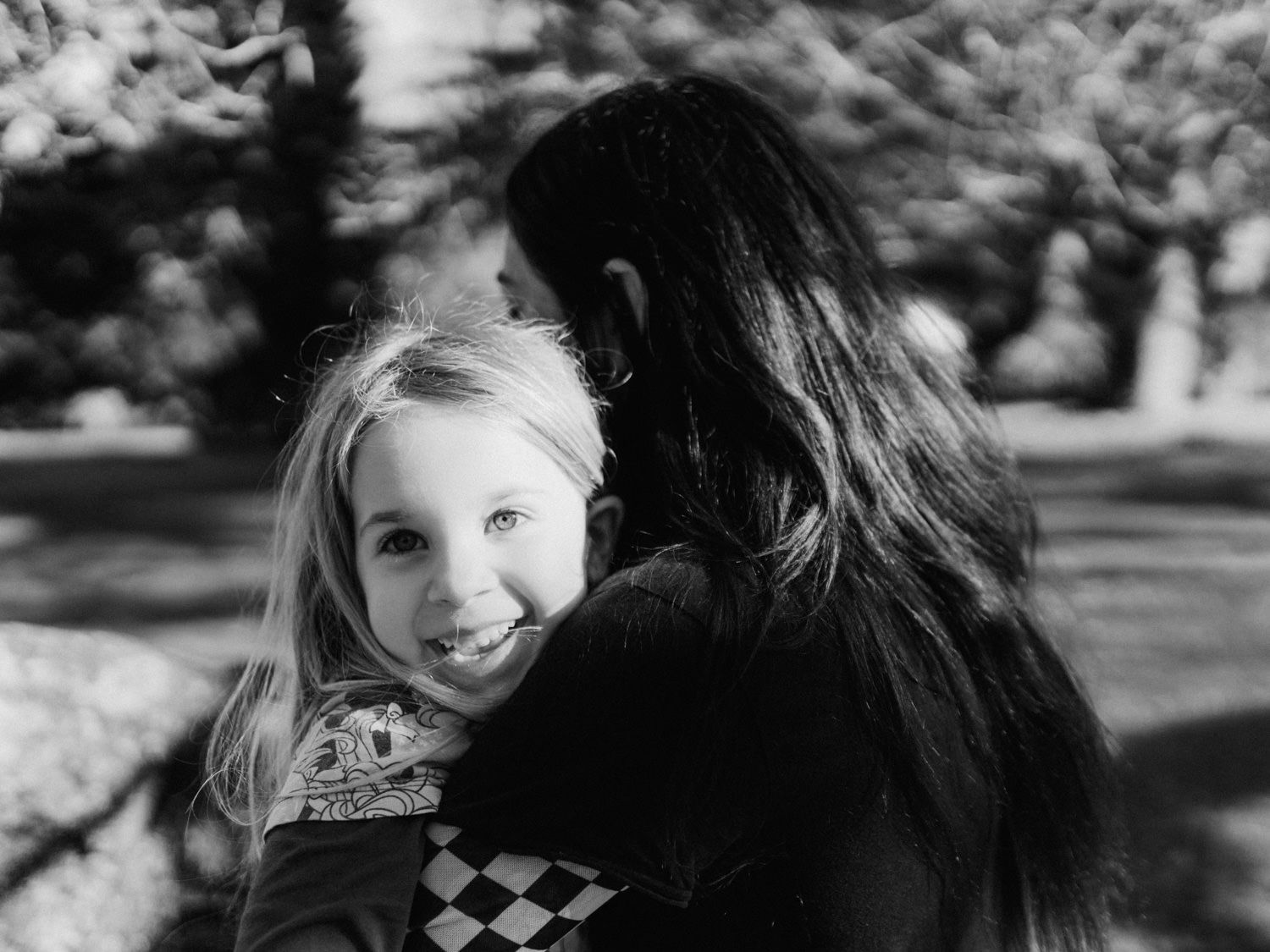 Black and white photo of a smiling young blonde girl being held by a dark-haired woman.