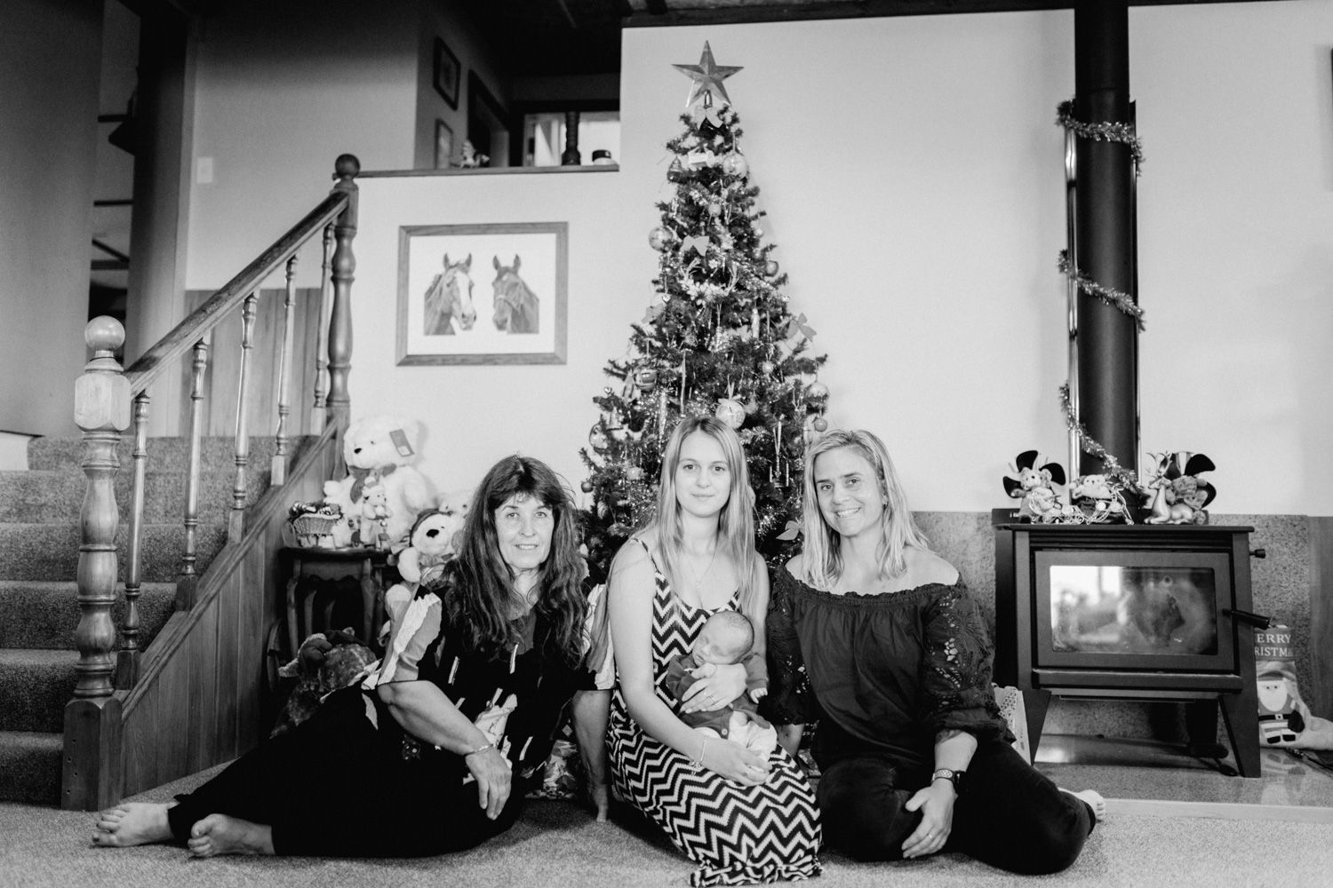 Three women sitting together in front of a decorated Christmas tree in a cozy home setting.