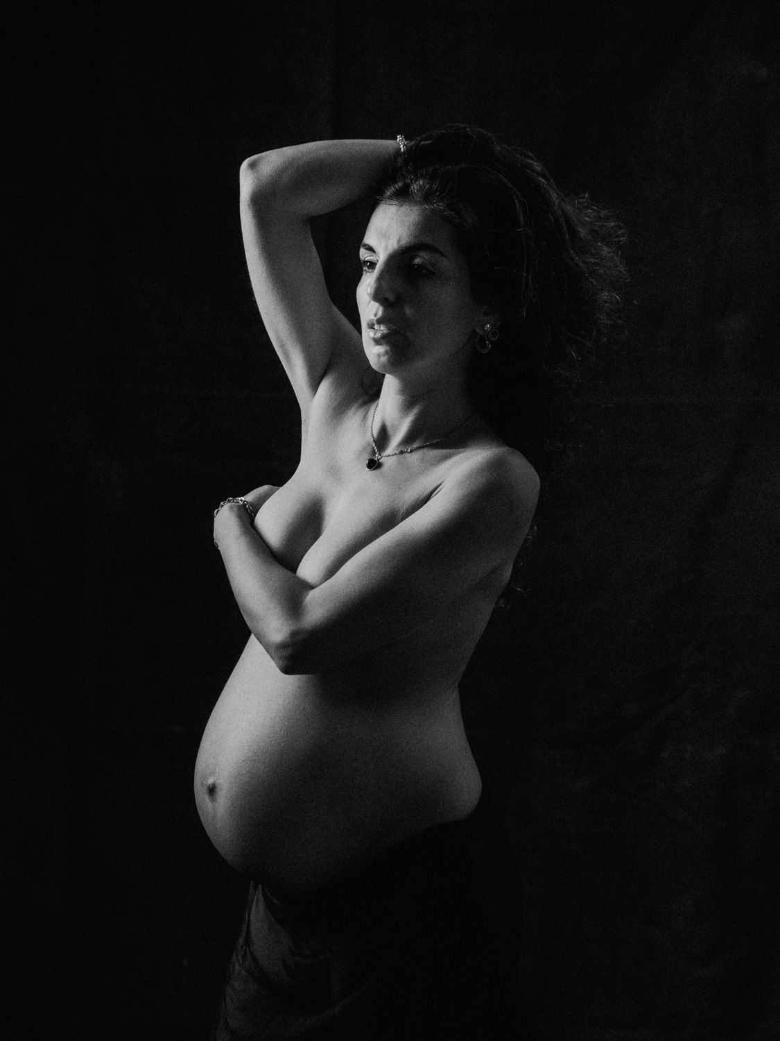 Black and white maternity portrait of a pregnant woman posing gracefully in dramatic studio lighting.