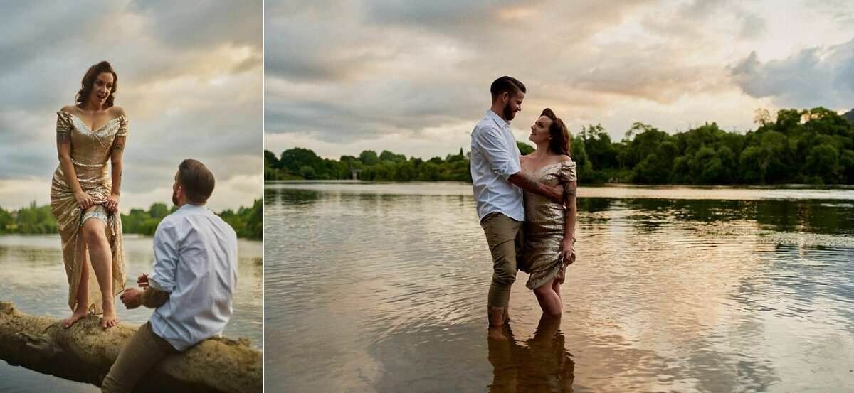 Couple sharing a romantic proposal and embrace by a serene river at sunset, surrounded by lush greenery.