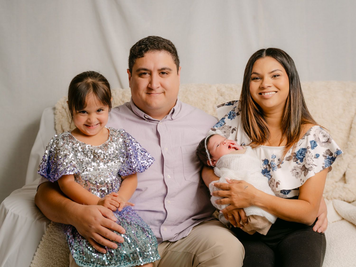 Happy family of four posing for a newborn portrait session, parents with toddler daughter and newborn baby.