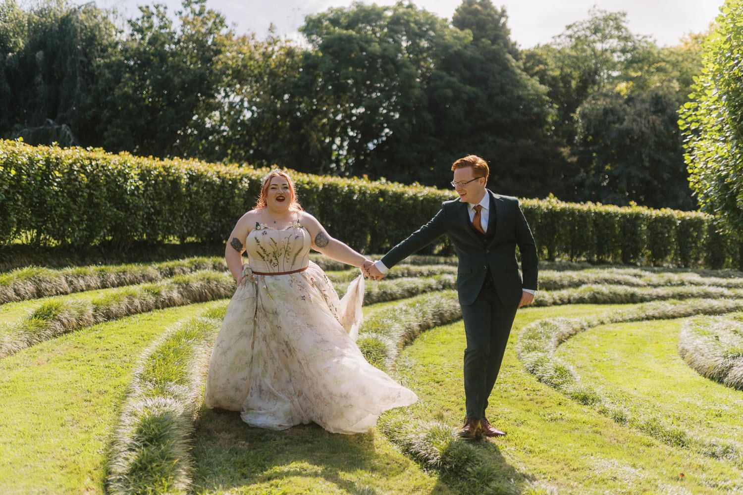 Bride and groom holding hands walking through a formal garden maze on their wedding day.