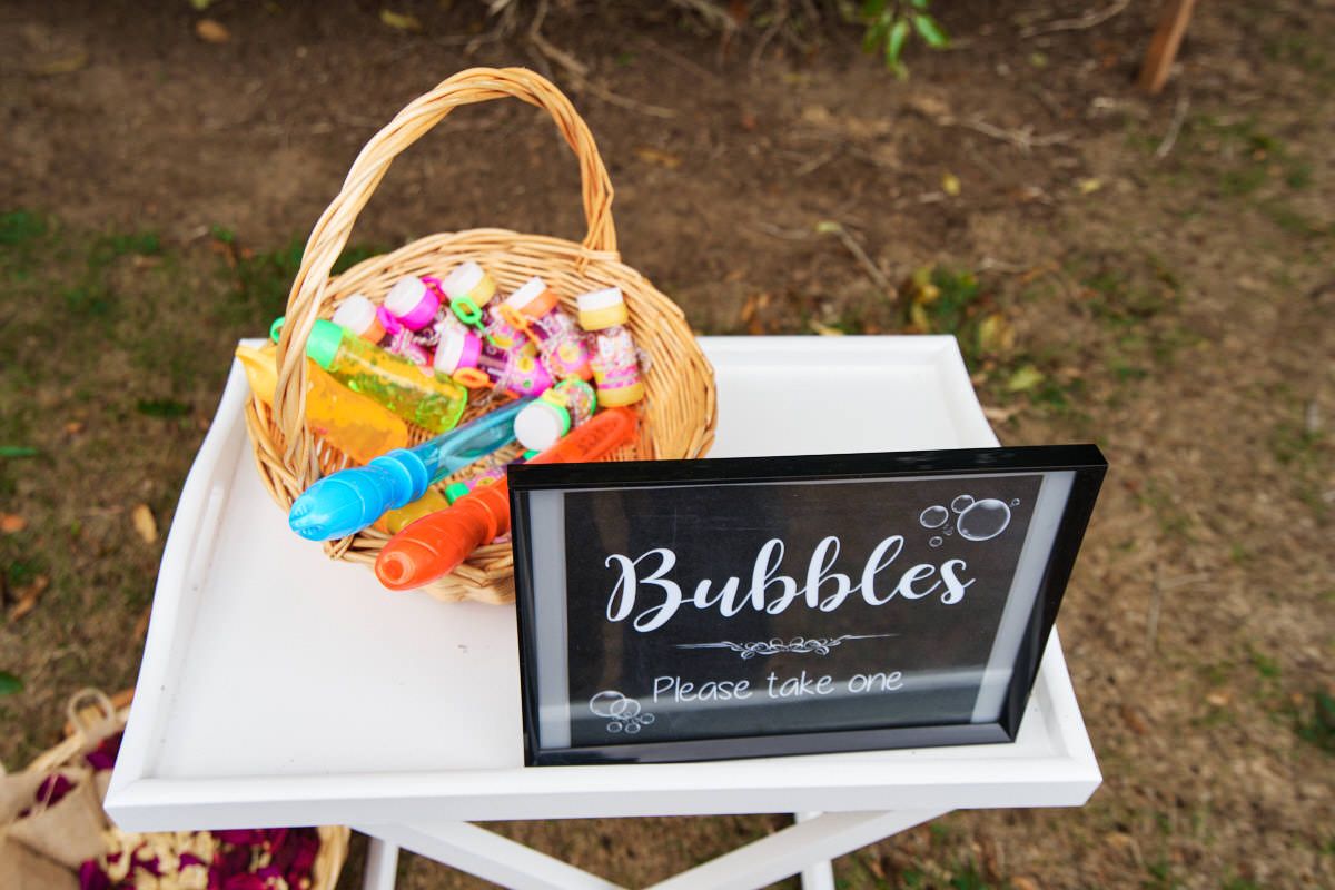 Wicker basket filled with colorful bubble wands next to a chalkboard sign reading Bubbles Please Take One on a white table.