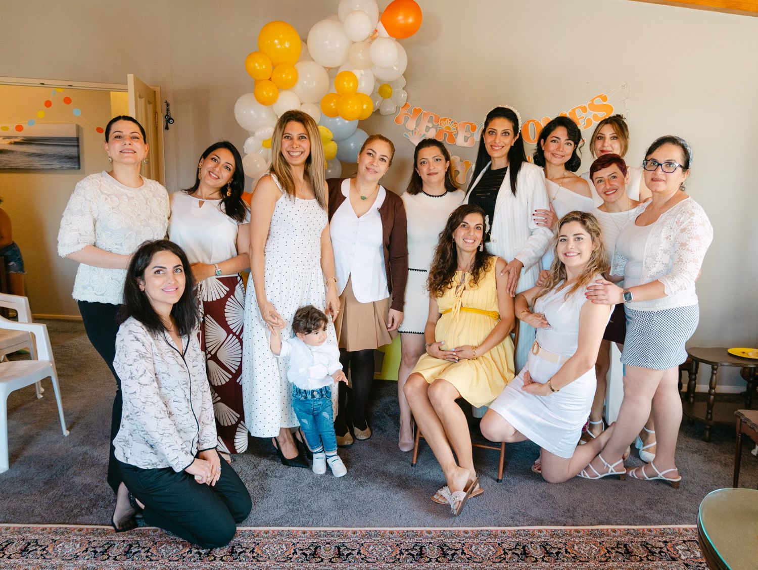 Group of women posing together at a baby shower with yellow and white balloon decorations.