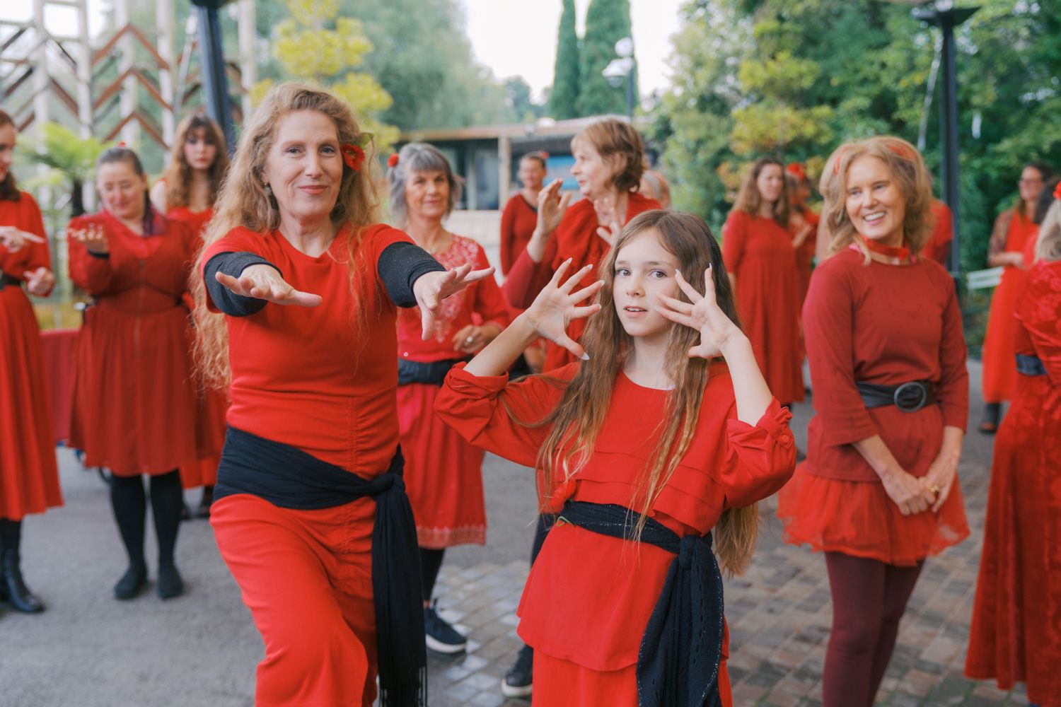 Group of women in matching red outfits performing a coordinated dance outdoors in a park setting.