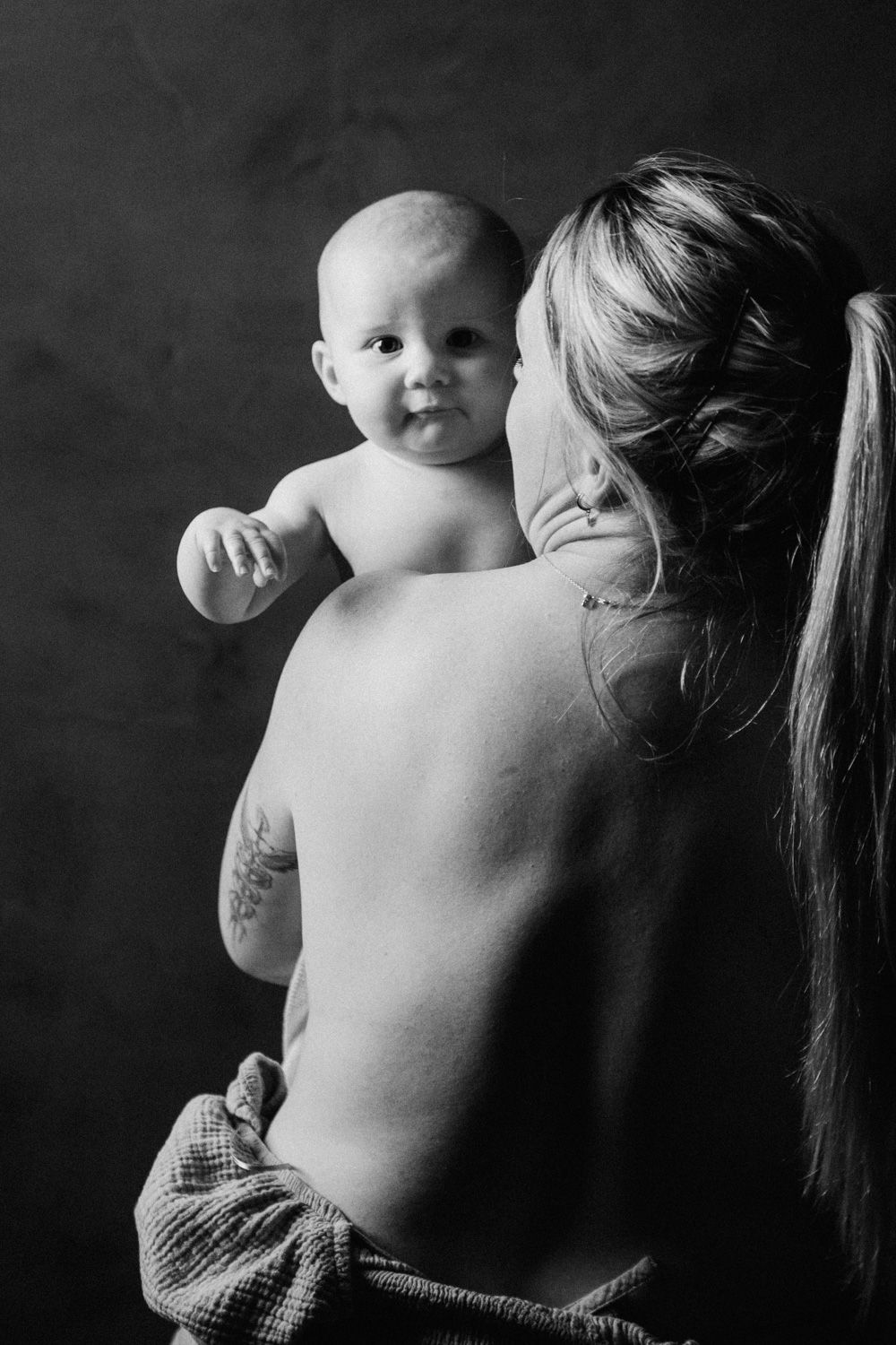 Black and white photo of a mother holding her smiling baby, showcasing a tender maternal bond in a studio setting.