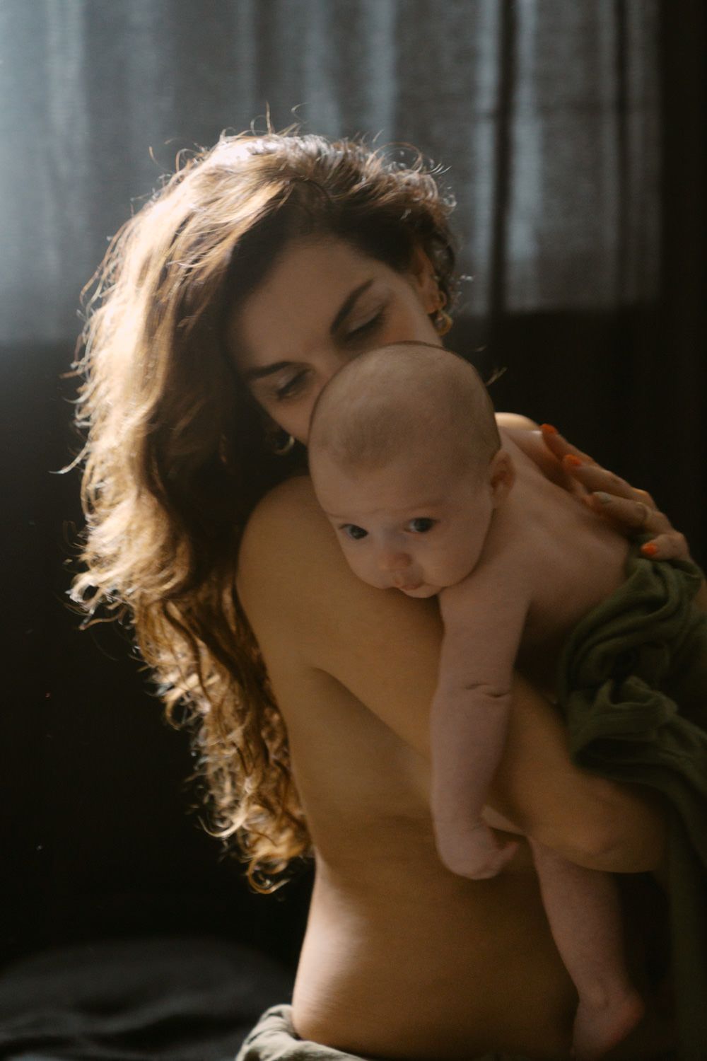 A mother tenderly holds her newborn baby close, sharing an intimate bonding moment in soft natural light.