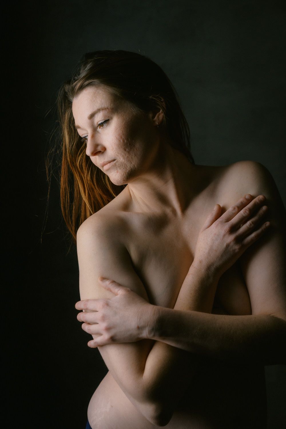 Woman with long hair posing with arms crossed over chest against dark background.