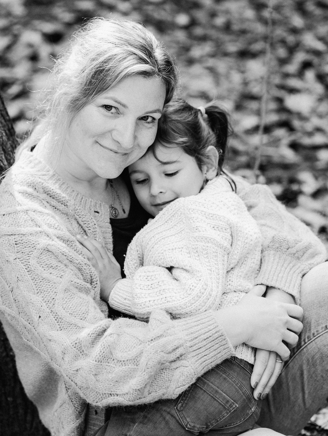Black and white photo of a smiling woman hugging a young girl in matching knit sweaters outdoors.