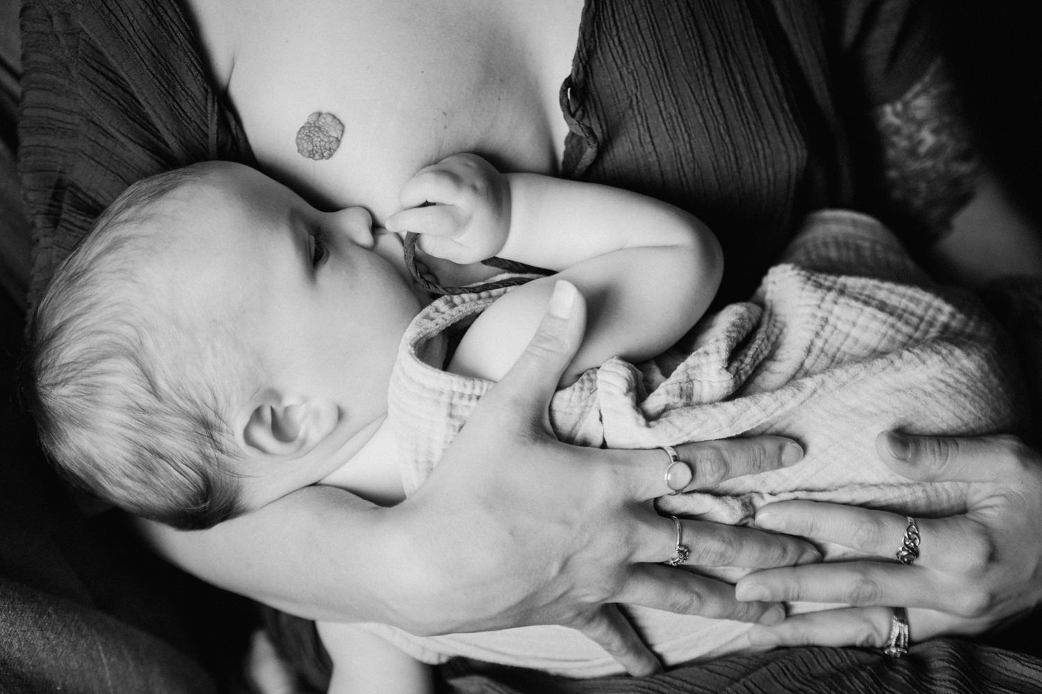 Black and white photo of a newborn baby breastfeeding while being cradled in mother's arms.