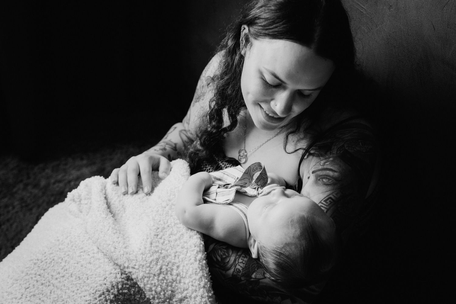 Black and white photo of a mother tenderly breastfeeding her newborn baby wrapped in a soft blanket.