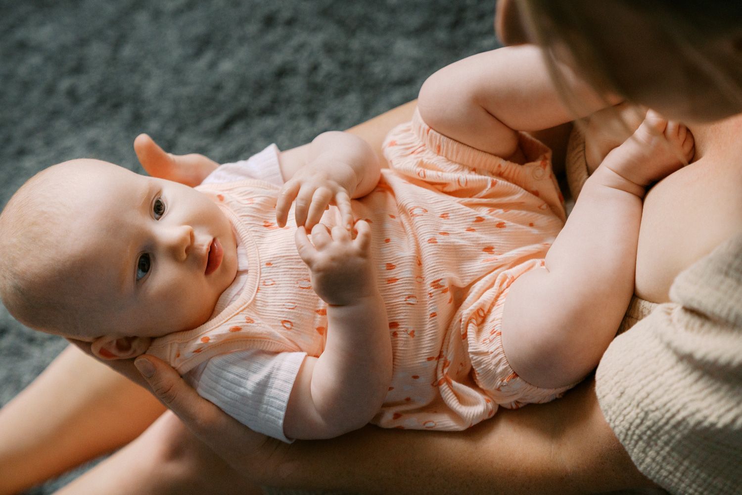 A mother gently holds her smiling baby dressed in an orange floral onesie during a tender bonding moment.