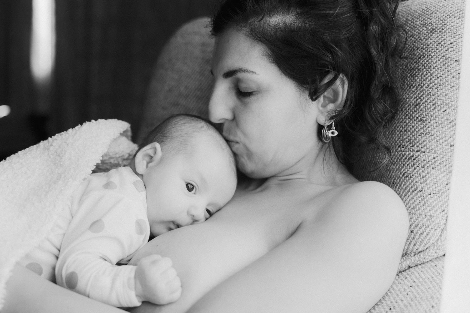 Black and white photo of a mother tenderly kissing her newborn baby while cradling them close.