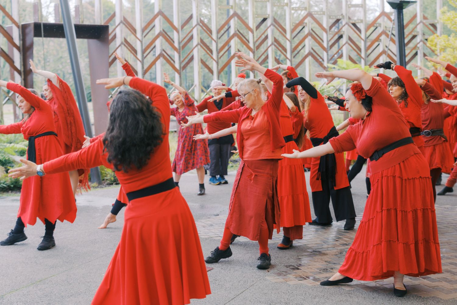 Group of women in red dresses dancing outdoors in a coordinated performance.
