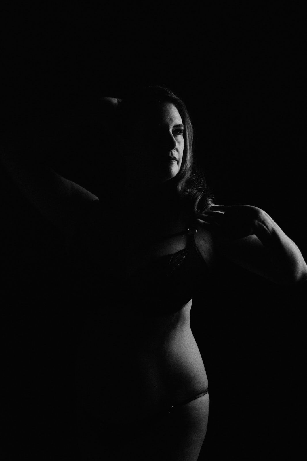 Black and white low-key portrait of a woman in lingerie posing gracefully against a dark background.