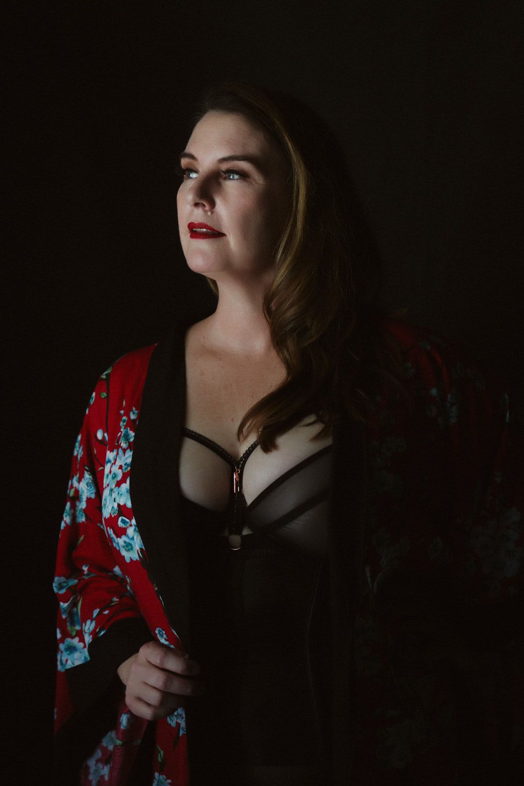 Woman in red floral kimono and black lingerie poses dramatically against dark background with red lips.