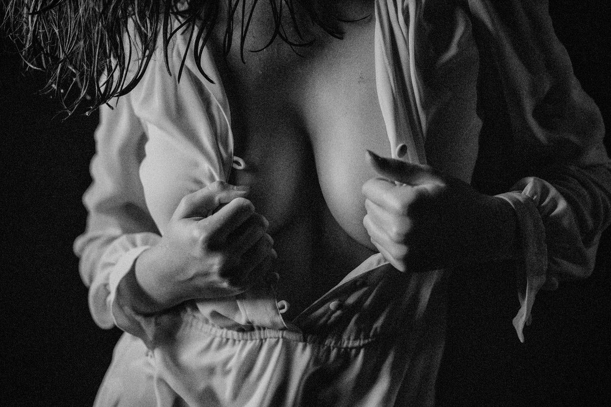 Black and white photo of a woman unbuttoning a white shirt, artistic boudoir photography.
