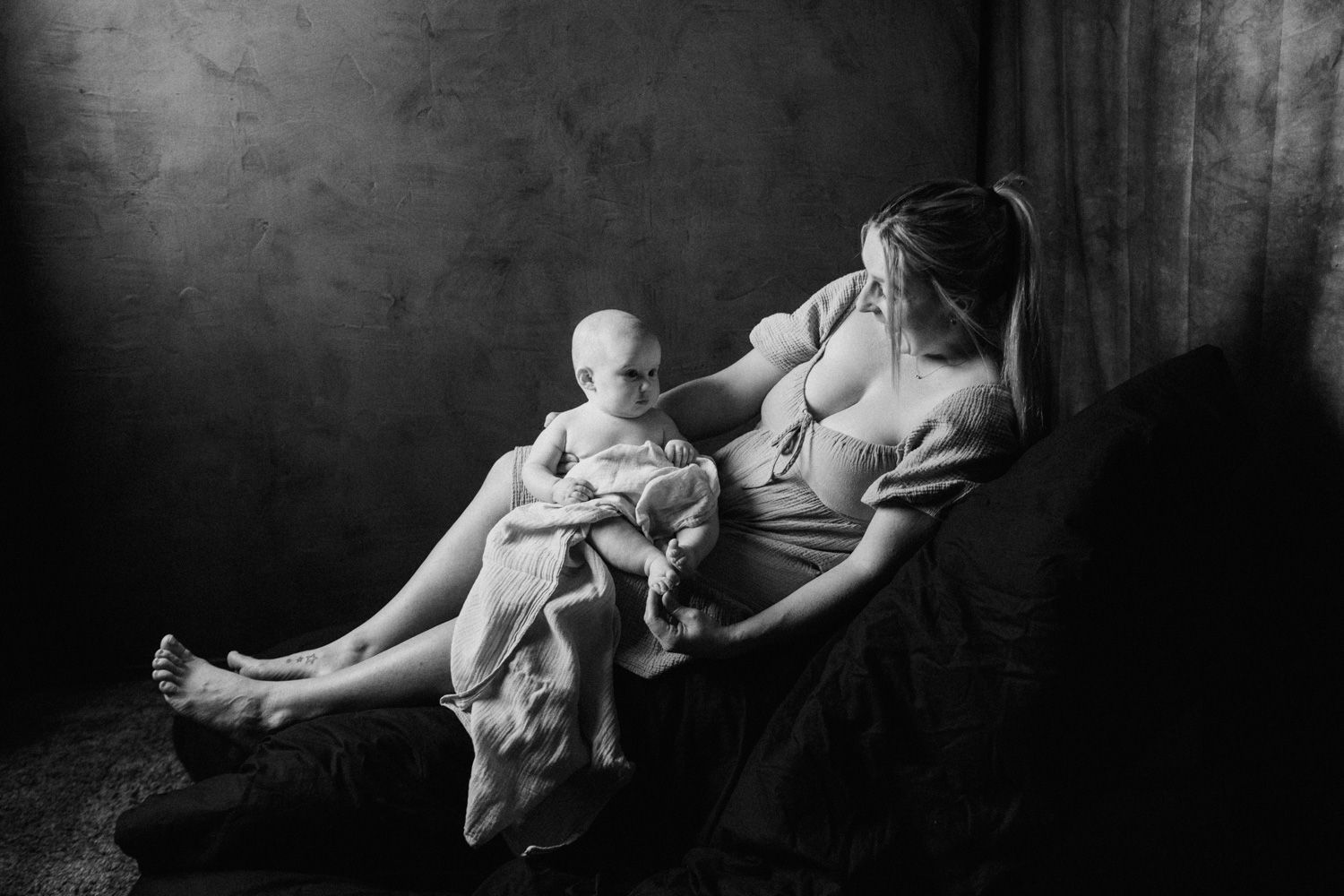 Black and white photo of a mother breastfeeding her baby while relaxing in a chair.