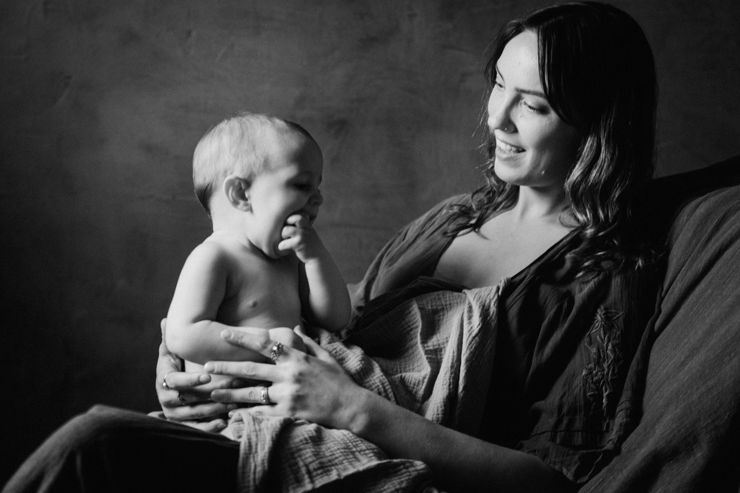 Black and white photo of a smiling mother laughing with her happy baby while seated in a chair.