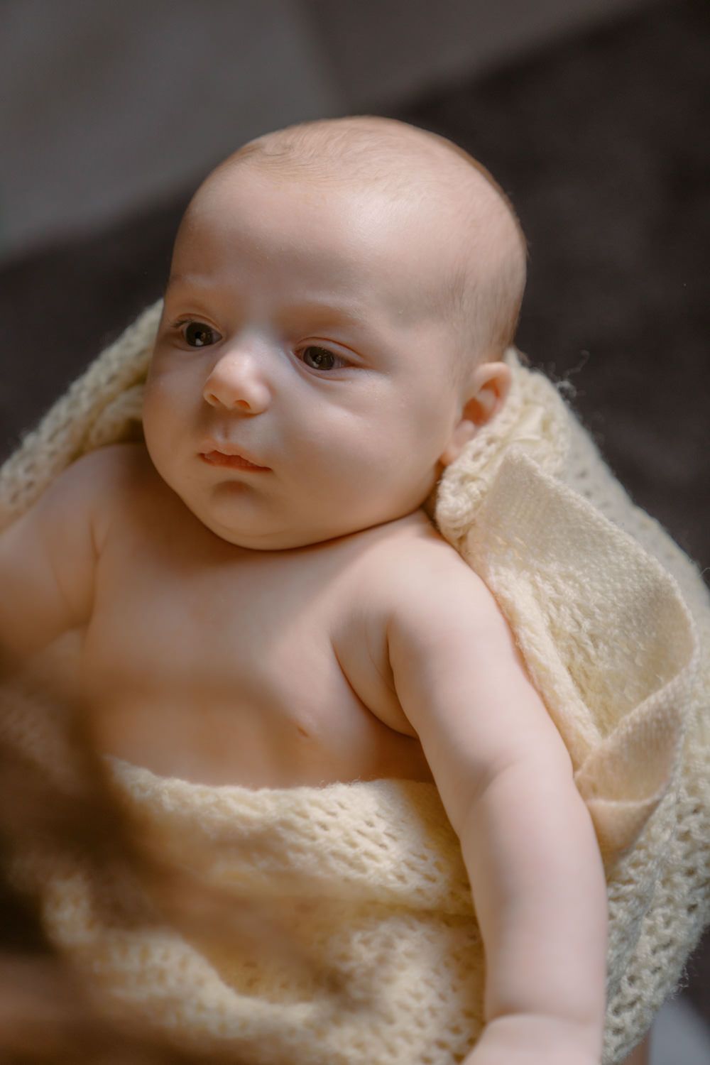 Newborn baby wrapped in a soft cream knit blanket, looking alert and peaceful.