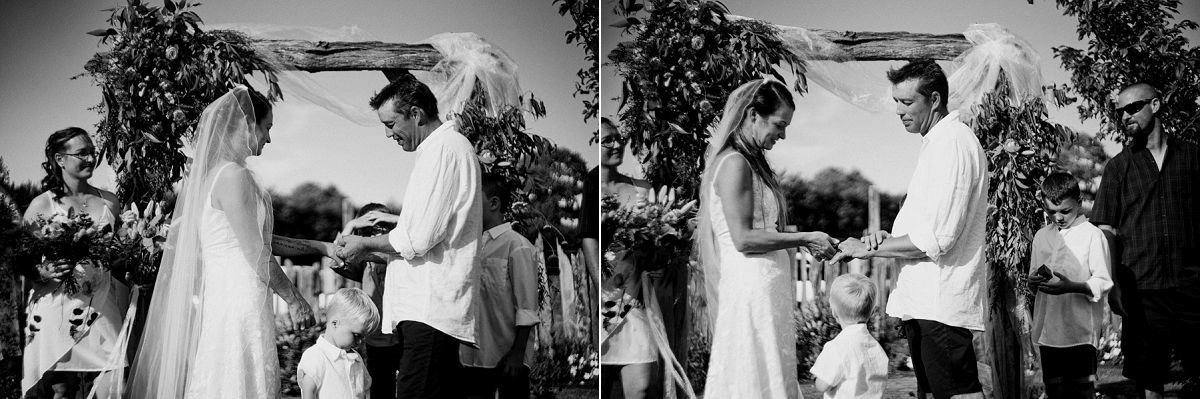 Black and white outdoor wedding ceremony with bride and groom exchanging vows under a floral arch.