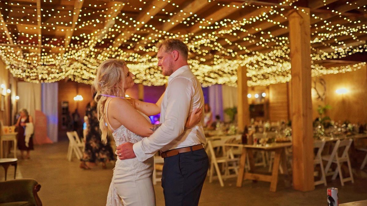 Couple sharing their first dance under twinkling fairy lights in a rustic wedding reception venue.