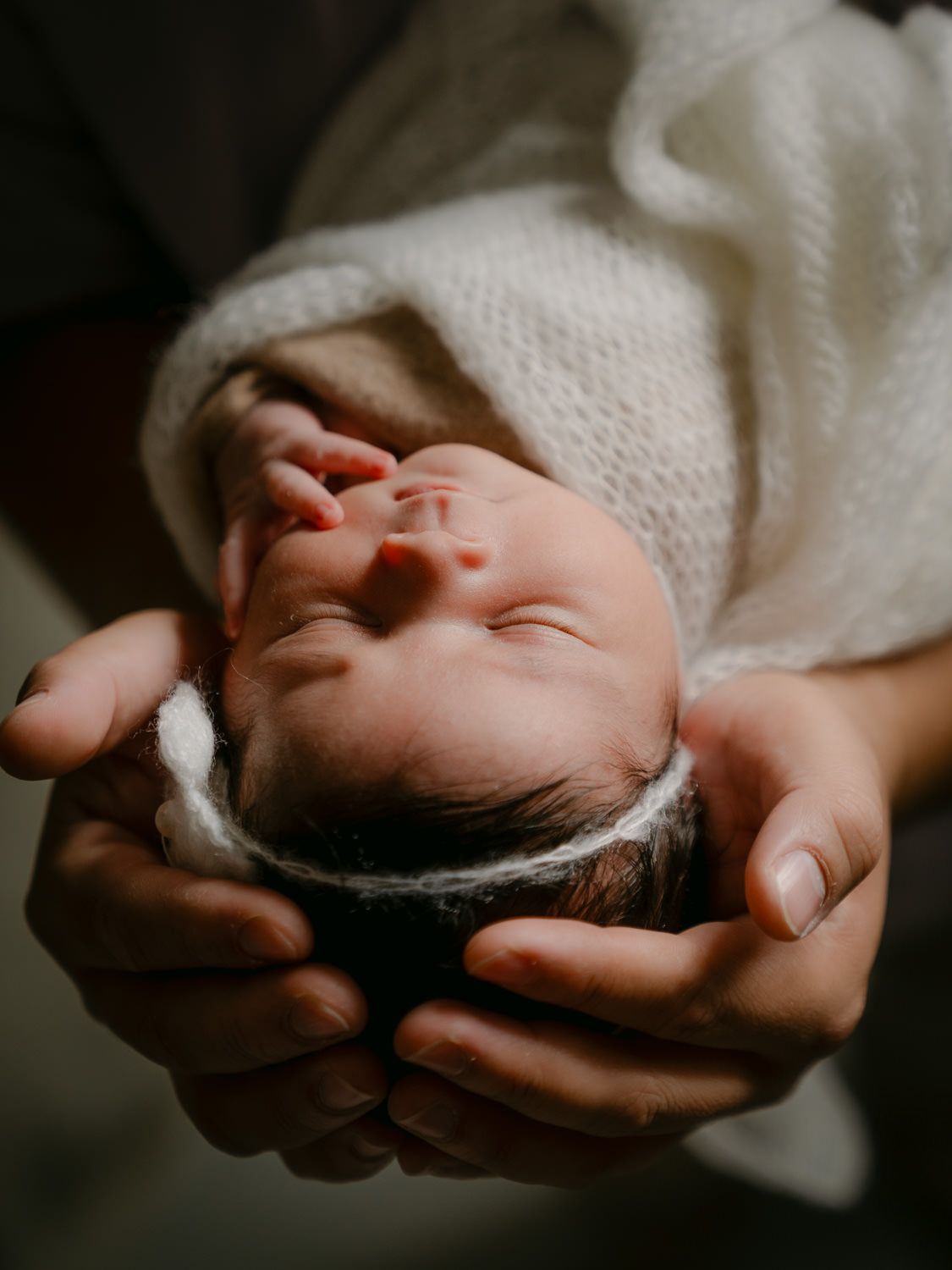 Newborn baby cradled gently in parent's hands, wrapped in a soft white knit blanket, peaceful and serene.