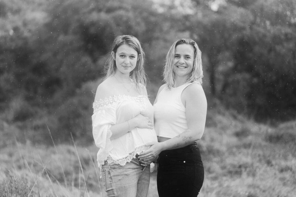 Two women smiling outdoors in a black and white portrait photo among natural greenery.