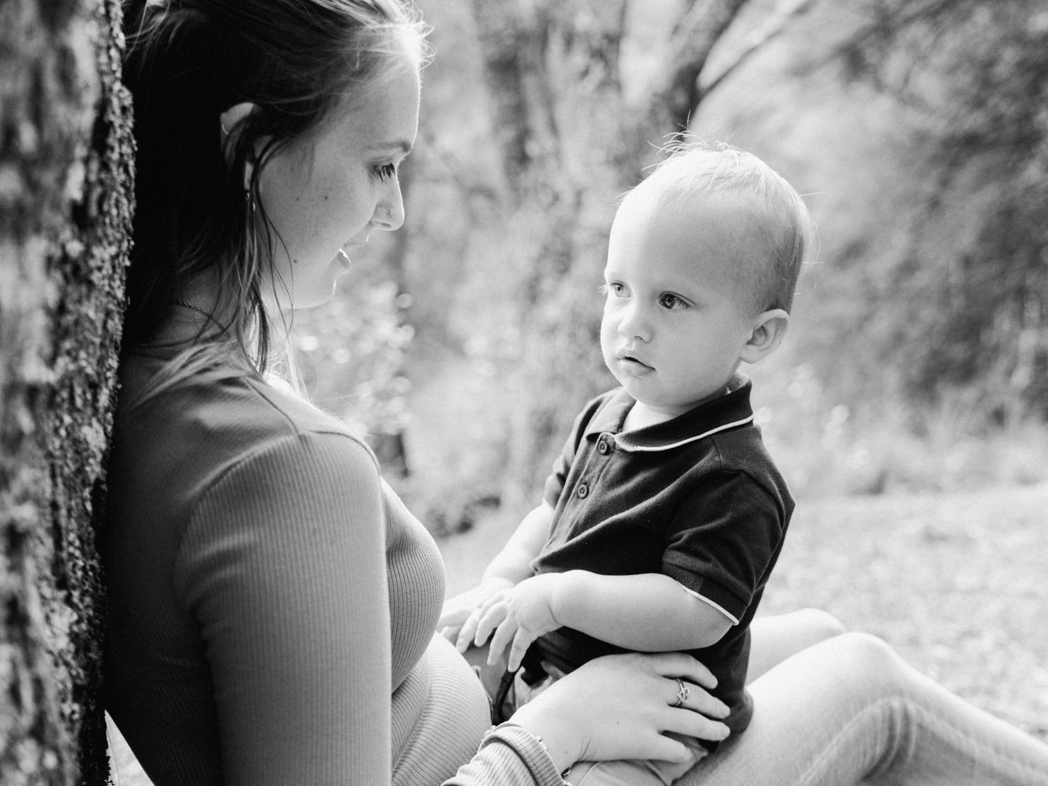 Black and white photo of a mother holding her young toddler son outdoors near a tree.