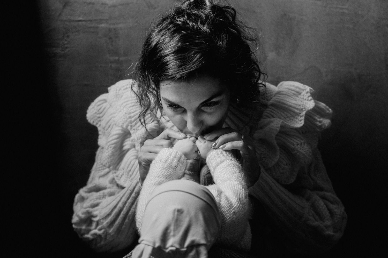 Black and white photo of a woman tenderly kissing a newborn baby wrapped in white cloth.