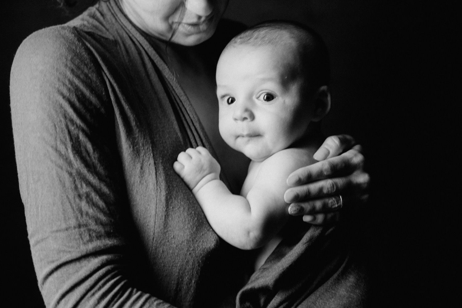 Black and white portrait of a mother tenderly holding her newborn baby against a dark background.