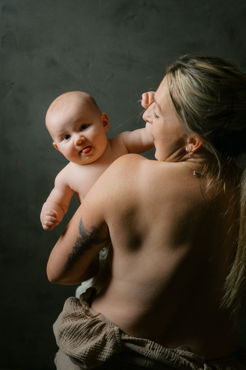 A mother holds her smiling baby up while sharing a tender moment against a dark studio background.