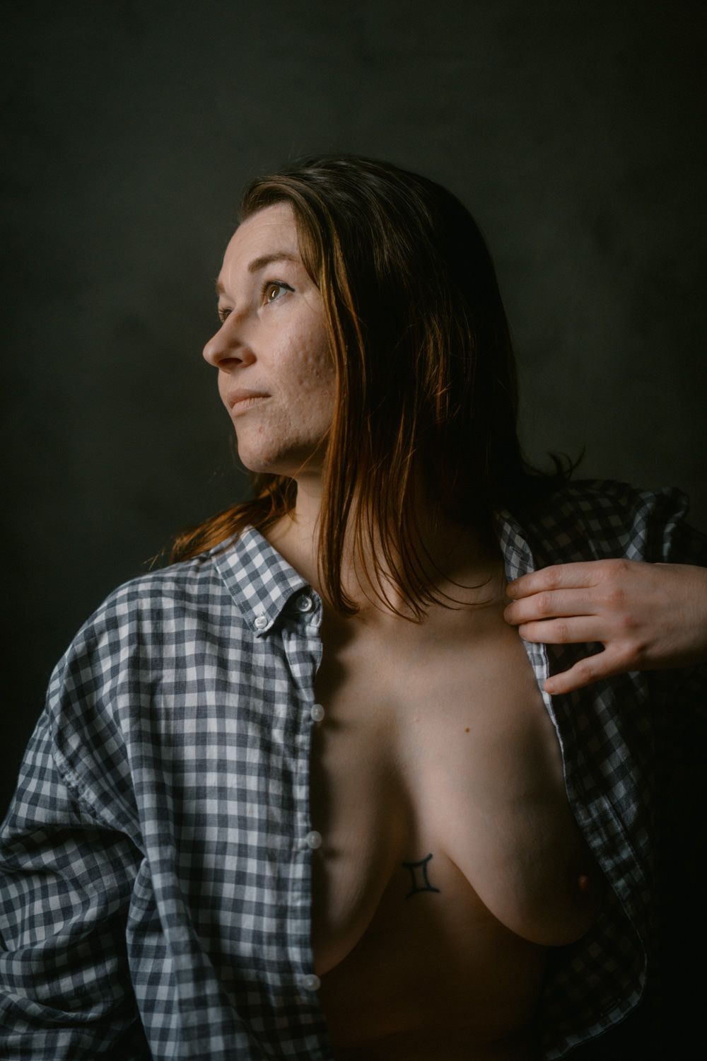 Woman in open plaid shirt posing in dramatic studio lighting against dark background.