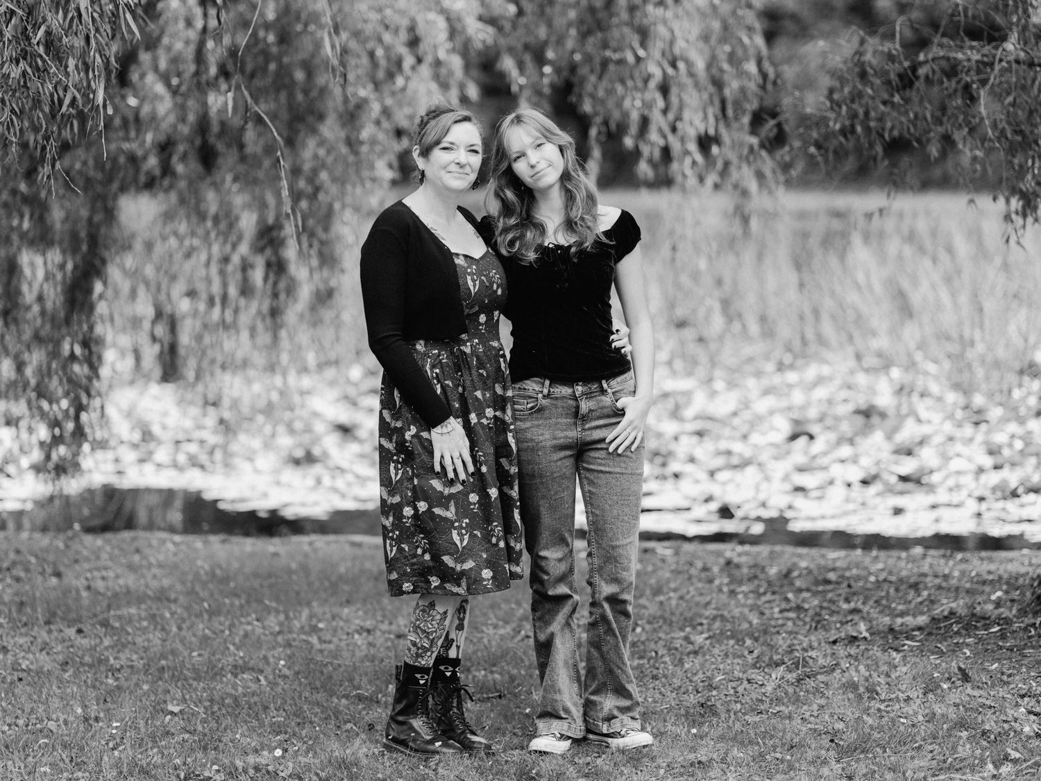 Black and white portrait of two women smiling outdoors near a tree and river backdrop.