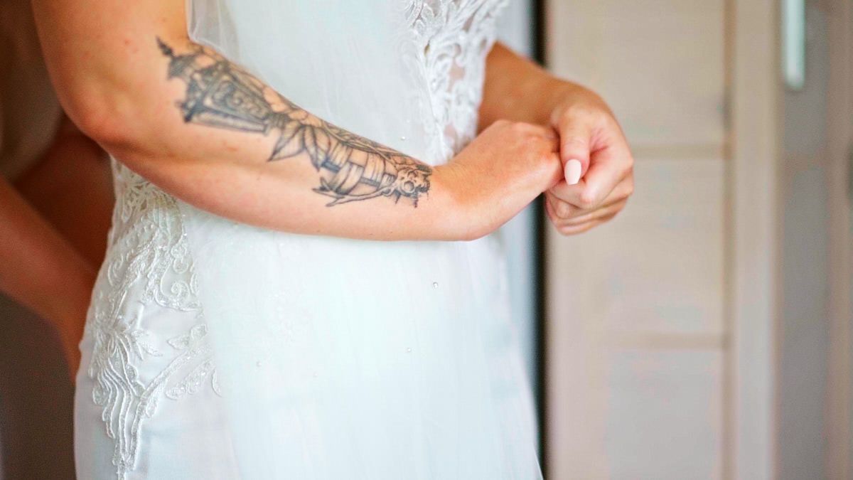 Tattooed bride in white lace wedding dress fastening her sleeve on her wedding day.