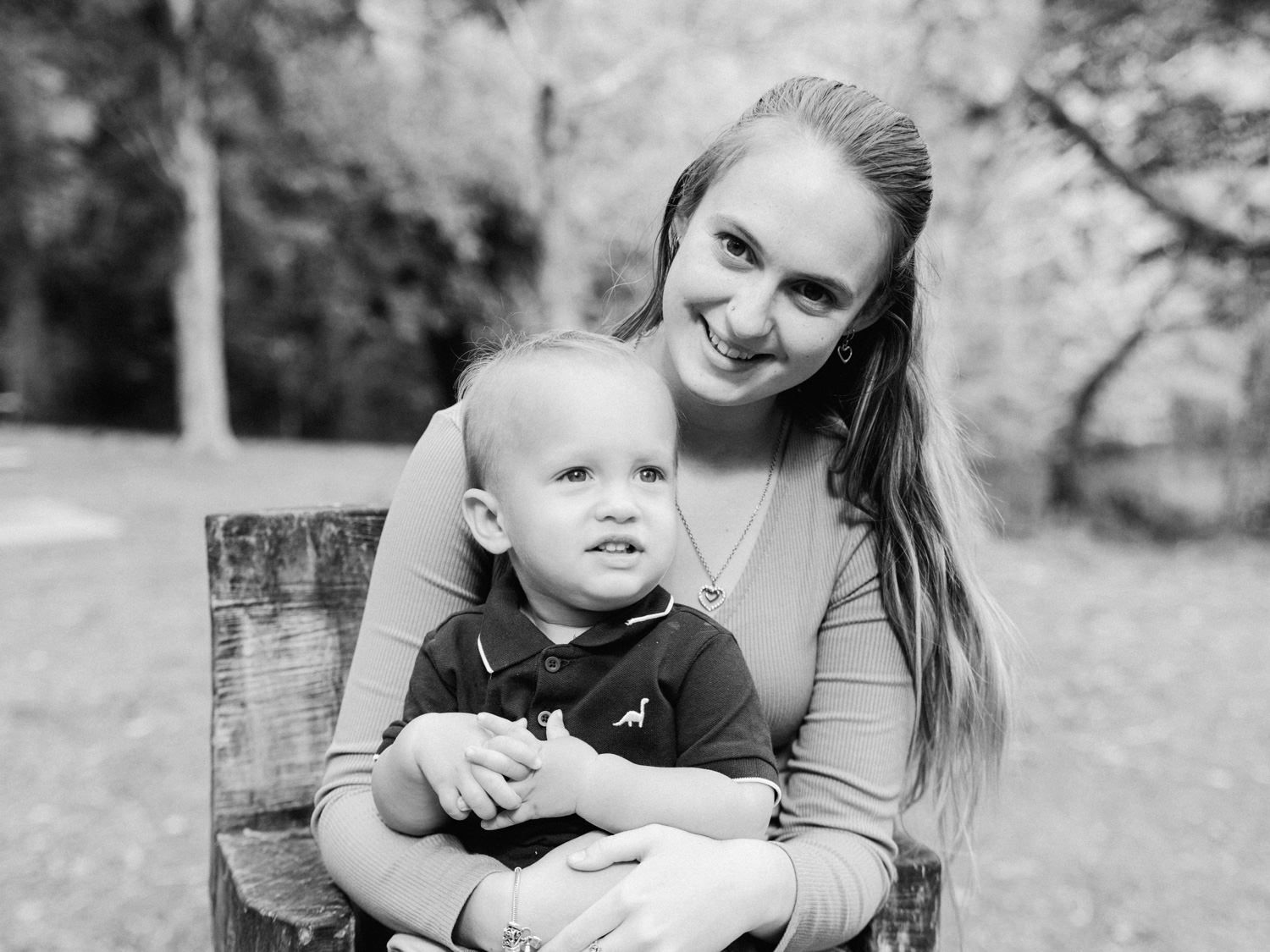 Black and white portrait of a smiling young woman holding a toddler boy on a bench outdoors.
