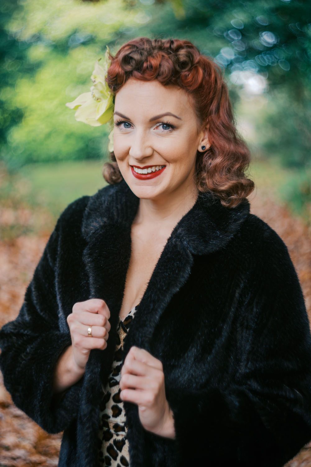Smiling redhead woman in vintage style with black fur coat and green hair accessory outdoors.