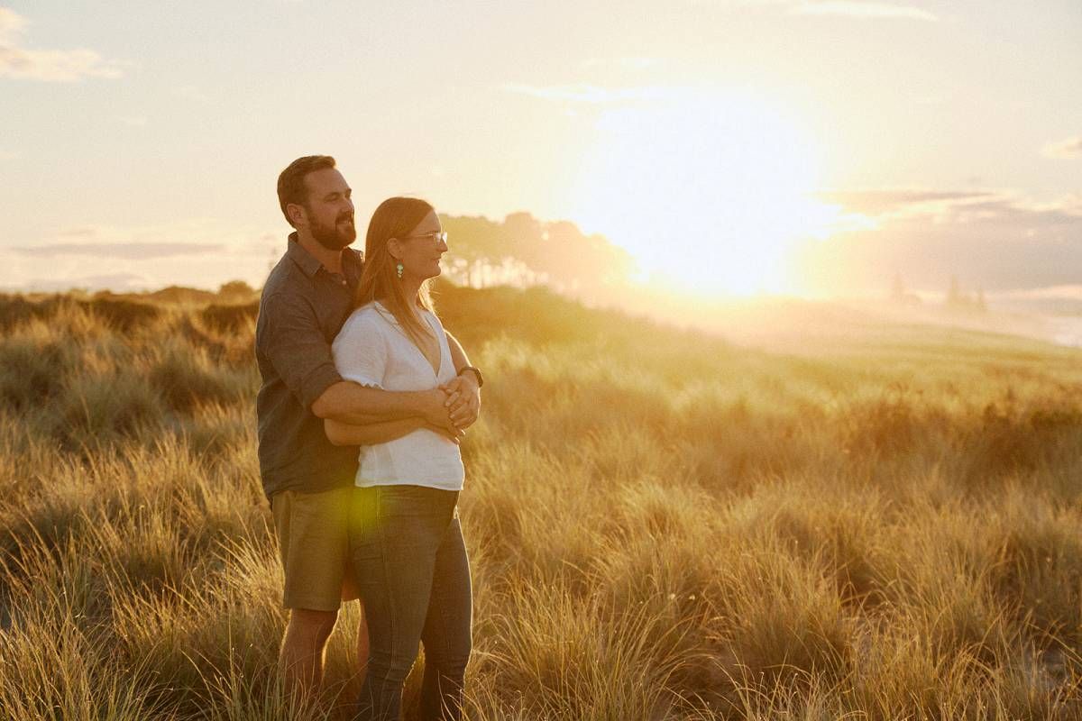 Couple embracing in golden sunset field, romantic outdoor portrait with warm sunlight glowing behind them.