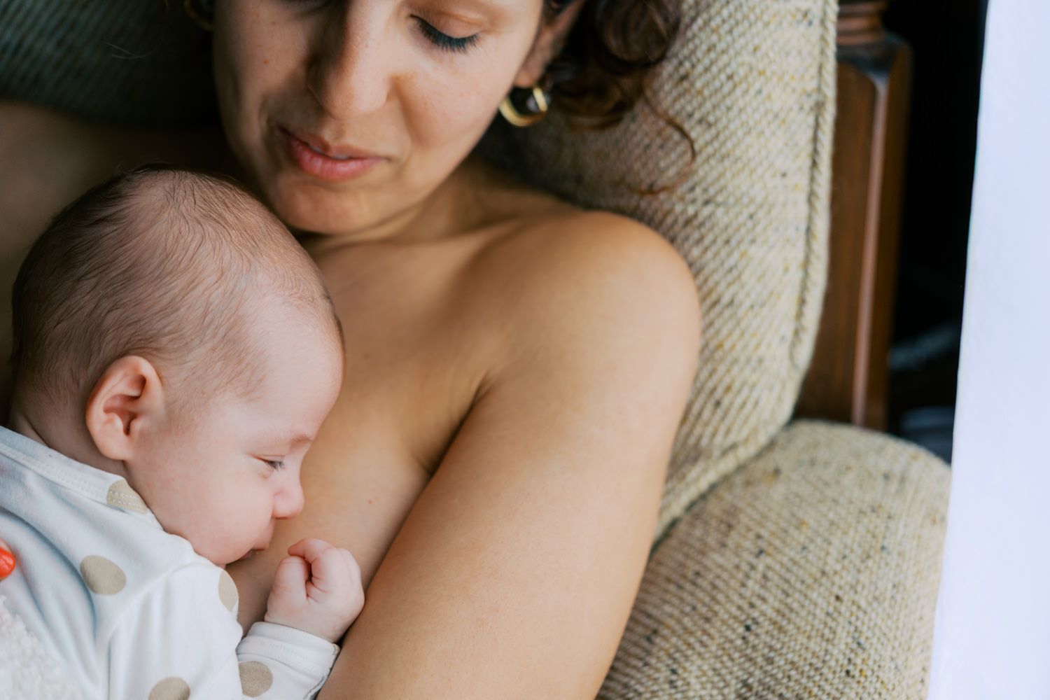 Mother breastfeeding her newborn baby while resting on a couch, sharing a tender bonding moment.