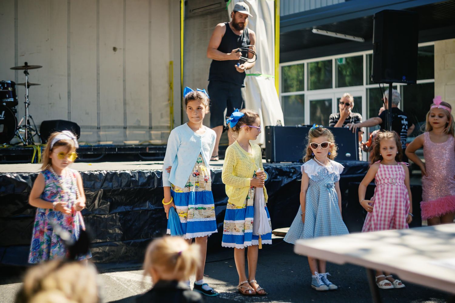 Young girls in colorful dresses performing on outdoor stage at community event.