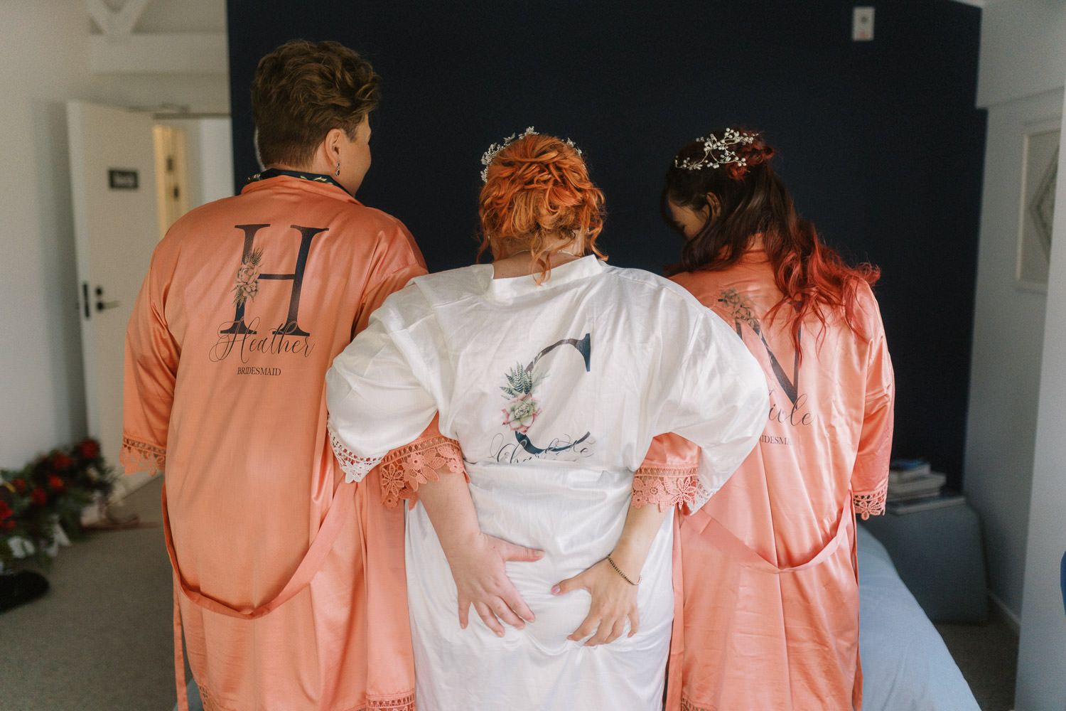 Bride and bridesmaids in coral satin robes preparing for wedding day getting ready photos.