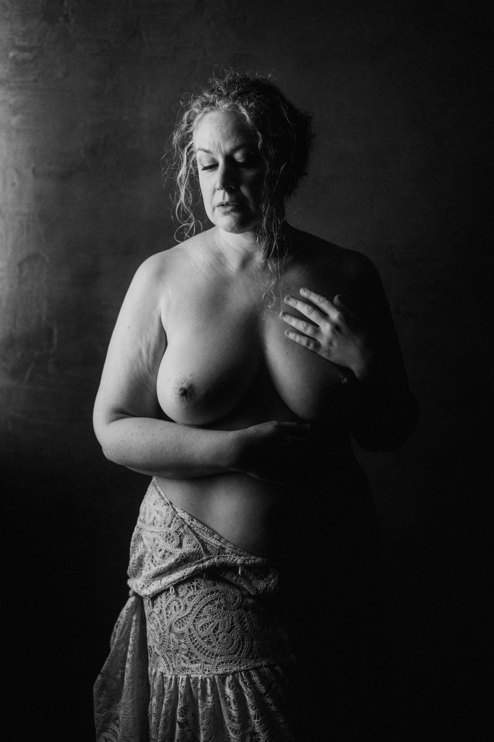 Black and white fine art portrait of a woman with curly hair posing topless, draped in lace fabric.