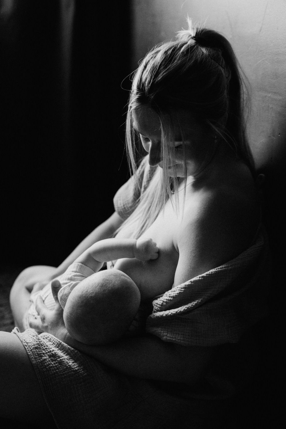 Black and white photo of a mother tenderly breastfeeding her newborn baby in soft natural light.