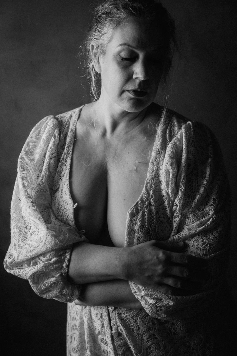 Black and white portrait of a woman in lace robe with arms crossed, looking down.
